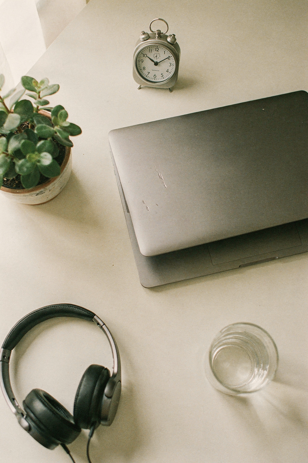 A laptop half closed, a small potted plant, a timer showing 3 minutes, a glass of water, noise-cancelling headphones. , no faces, no hands