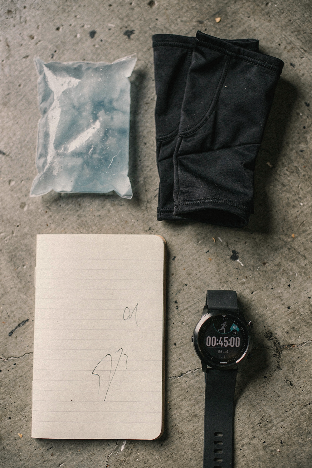 An unused ice pack, compression boots folded neatly, a simple lined notebook open with writing, and a digital watch showing a timer. , no faces, no hands
